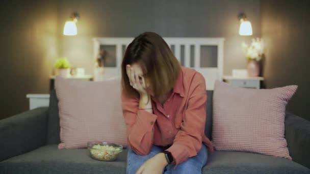 Traurige und enttäuschte Frau sitzt auf dem Sofa und schaut fern — Stockvideo