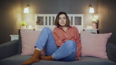 Genç bir kadın kanepede oturur ve televizyon izler. Kameraya bak.