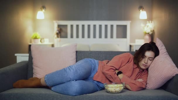 Молодая женщина спит на диване с попкорном — стоковое видео