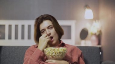 Sıkıcı bir kadının kanepede oturup patlamış mısır yiyip televizyon izlemesi.