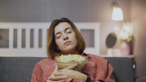 CLose up de jeune femme assise sur le canapé, manger du pop-corn, regarder la télévision et tomber alseep — Video