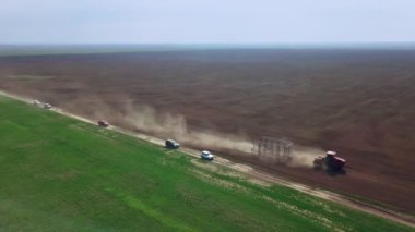 Bir traktörde tohum eken çiftçi tarlaya tahıl ekimi için toprağı hazırlıyor. Toz toprağına tohum ekiyorum. Bahar tarım işi. Hava görüntüsü, insansız hava aracı öne doğru uçar traktörü takip eder