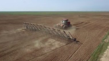 Büyük bir kanca kuvvetiyle enerji dolu güçlü bir traktörün hava görüntüsü, sonbaharda kış ekinleri için bir disk ekiciyle ekin ekiyor.