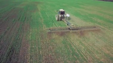 Büyük bir kanca kuvvetiyle enerji dolu güçlü bir traktörün hava görüntüsü, sonbaharda kış ekinleri için bir disk ekiciyle ekin ekiyor.