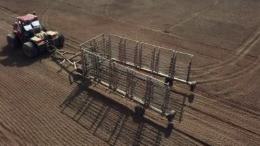 Bir traktörde tohum eken çiftçi tarlaya tahıl ekimi için toprağı hazırlıyor. Toz toprağına tohum ekiyorum. Bahar tarım işi. Hava görüntüsü, insansız hava aracı öne doğru uçar traktörü takip eder