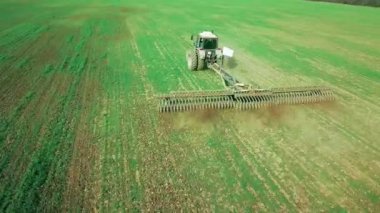 Tarlalarda arazi hazırlayan traktördeki bir çiftçinin hava görüntüsü. Beyaz traktör tarlaları sürüyor, toprağı ekime hazırlıyor..