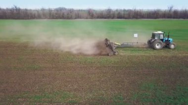 Büyük bir kanca kuvvetiyle enerji dolu güçlü bir traktörün hava görüntüsü, sonbaharda kış ekinleri için bir disk ekiciyle ekin ekiyor.