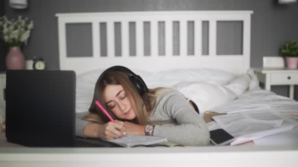 Ung kvinna med hörlurar liggande på sängen och gör heta på bärbara datorer — Stockvideo