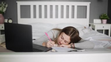 Tembel kız öğrenci yatakta uzanıyor ve evde çalışıyor, online eğitim alıyor.
