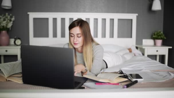 Mujer joven acostada en la cama escribiendo en el portátil y utilizando el teléfono inteligente — Vídeo de stock