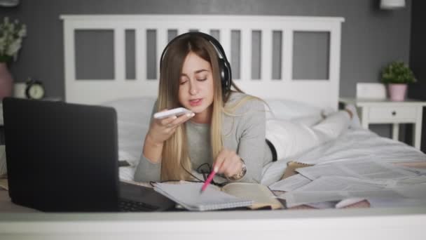 Young woman work at home. Woman lays on the bed and records audio voice message — Stock Video