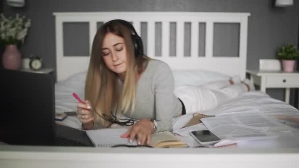 A fiatal diáklány jegyzetfüzetbe ír. Az ágyon távoktatás a diákok számára. Koronavírus. Karantén. Egy nő laptopot néz. Szabadúszó, távoli munka, otthoni munka, online oktatás — Stock videók