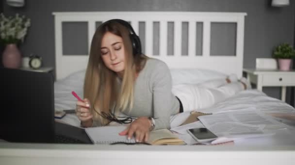 Young female student writes in notebook. On the bed distance learning for students. Coronavirus. Quarantine. Woman look at a laptop computer. Freelancer, distant work, work at home, online education — Stock Video