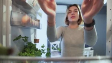 Buzdolabının İçinden Dışarıya Bakarken Kadın tabağı patates kızartması ile açar sonra geri koyar ve bir elma alır.