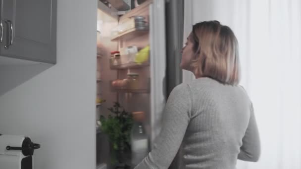 La mujer abre la puerta del refrigerador en la cocina en casa y toma manzana — Vídeos de Stock