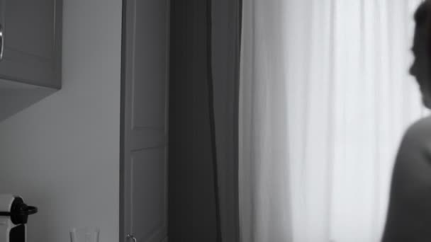 Женщина с головным убором или похмельем открывает дверь холодильника на кухне дома и берет бутылку воды — стоковое видео