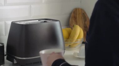 Siyah pijamalı genç bayanın sabah kahvaltısını hazırladığı yakın plan. Kadın pembe fincana sıcak su döker.