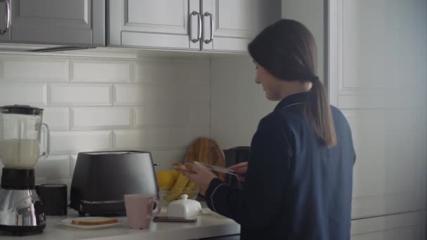 Mujer joven en pijama negro preparando el desayuno por la mañana. Mujer extiende mantequilla en pan tostado — Vídeos de Stock