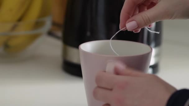 Mulher coloca saco de chá em uma xícara rosa com uma água quente — Vídeo de Stock