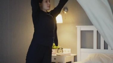 Siyah pijamalı genç bir kadın yatak odasını topluyor.