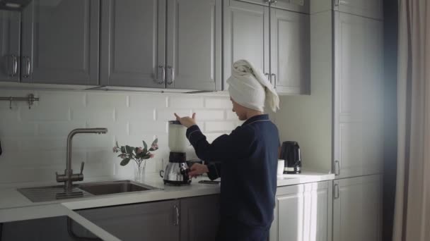 Mujer joven en pijama negro preparando el desayuno por la mañana. Mujer hace un cóctel en una licuadora y utiliza el teléfono inteligente — Vídeo de stock