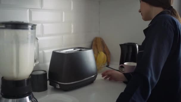 Primer plano de la joven en pijama negro preparando el desayuno por la mañana. Mujer enciende la tostadora, Hervidor eléctrico y hace un cóctel en una licuadora — Vídeos de Stock