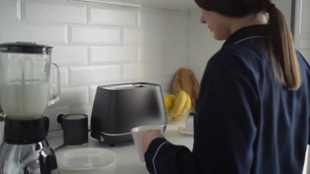 Mujer joven en pijama negro preparando el desayuno por la mañana. Mujer vierte un agua caliente a la taza — Vídeos de Stock