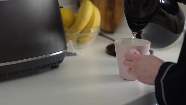 Vrouw giet warm water in een roze kopje en zet theezakje — Stockvideo