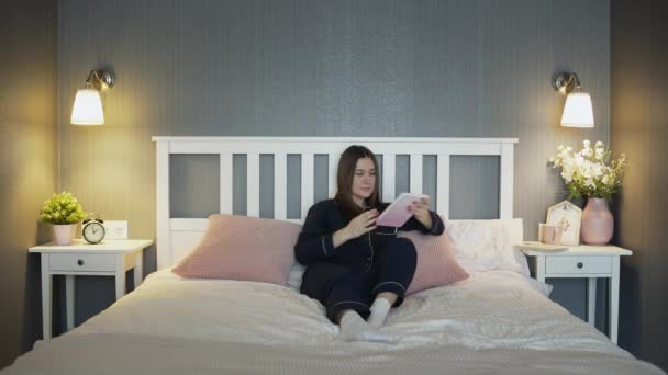 Νεαρή γυναίκα με μαύρες πιτζάμες διαβάζει βιβλίο στο κρεβάτι στο σπίτι — Αρχείο Βίντεο