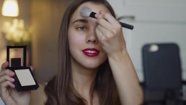 Porträtt bild av den unga vackra kvinnliga skönhet video bloggare lära hur man gör makeup och göra hennes panna och kinder med pulver framför kameran. — Stockvideo