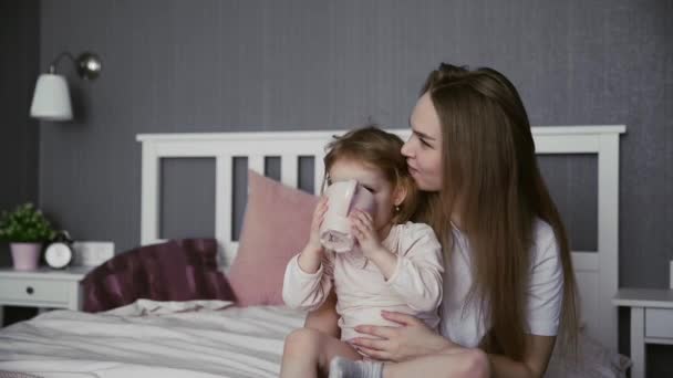Jovem mãe e sua filha se senta na cama e bebe água — Vídeo de Stock
