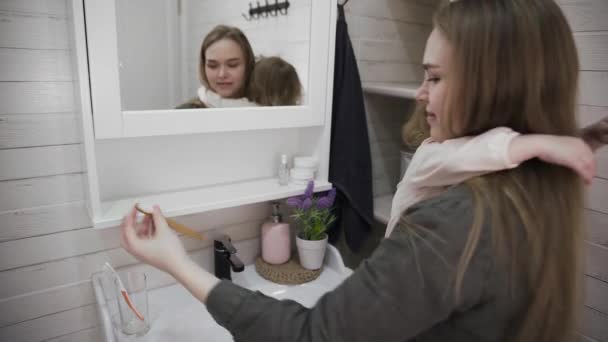 Молода приваблива мама і її мила дочка пробує чистити зуби перед дзеркалом . — стокове відео