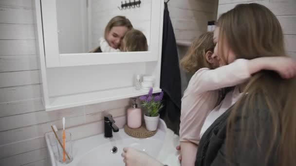 Joven atractiva mamá y su linda hija intenta cepillarse los dientes delante del espejo . — Vídeo de stock