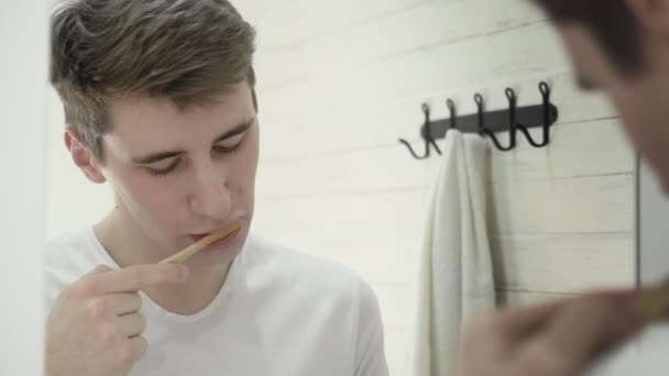 Молодий чоловік тримає дерев'яну щітку чистити зуби, дивлячись на телефон — стокове відео