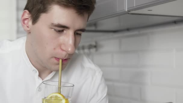 Young man in a white short uses reusable eco-friendly ecological bamboo straw to drink water with lemon at the kitchen — Stock Video