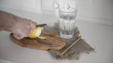 Bir adam ahşap masada limon keser ve limon dilimini suyla bardağa koyar.