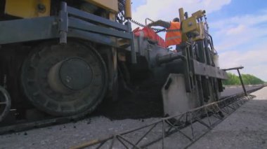 Yeni yolda taze asfalt var. Yol yapımı. Yol yapımı ve tamirat sırasında asfalt kaldırım taşı makinesi. Üniforma geçmişi olan işçiler