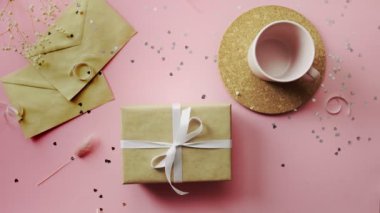 Kadın eli, beyaz kurdeleyle sarılmış bir Noel hediyesine dokunuyor. Tahta, pembe masa, düz uzanma.