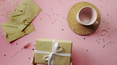 Kadın elleri, el sanatları kağıdına sarılmış beyaz kurdeleli Noel hediyesini ahşap masanın üstüne koyuyor.