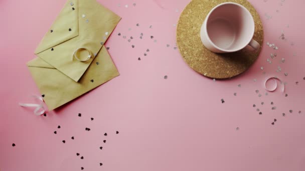 Manos de mujer dando un regalo de Navidad envuelto en papel artesanal con lazo blanco. Vista superior sobre tabla rosada de madera, posición plana — Vídeos de Stock