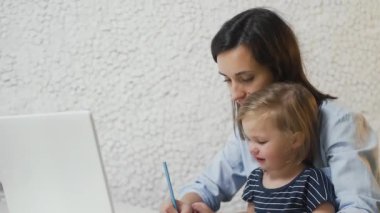 Genç anne bebeğine şişeden meyve suyu veriyor ve defter üzerinde çalışıyor.