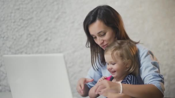 Mère qui travaille avec bébé à table. Femme occupée travaillant sur un ordinateur portable avec une petite fille sourit et rit sur les mains . — Video