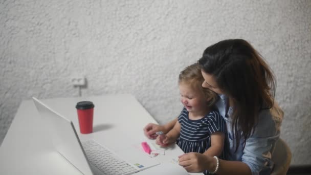 Een vrouw die een kind afleidt en verder werkt aan een notitieboekje. Jonge vrouw kalmeert huilen kind in het kantoor. — Stockvideo