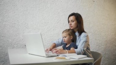 Genç bir kadın defter üzerinde çalışıyor ve çocuğuna ekranda bir şey gösteriyor.