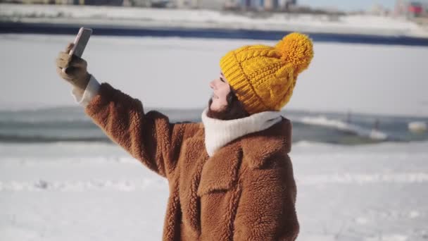 Jovem com aparelho nos dentes em casaco de pele leva uma selfie ao ar livre — Vídeo de Stock