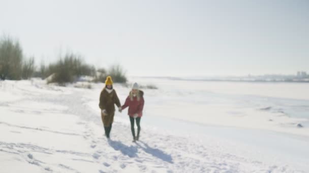 Två kvinnliga vänner håller varandra i händerna och springer på snön — Stockvideo