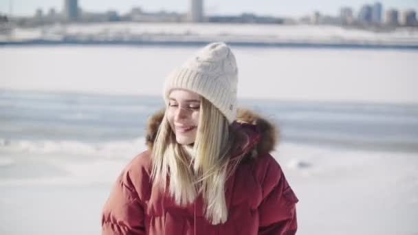 Ung kvinna i vit stickad hatt och röd vinterjacka poserar på kameran — Stockvideo