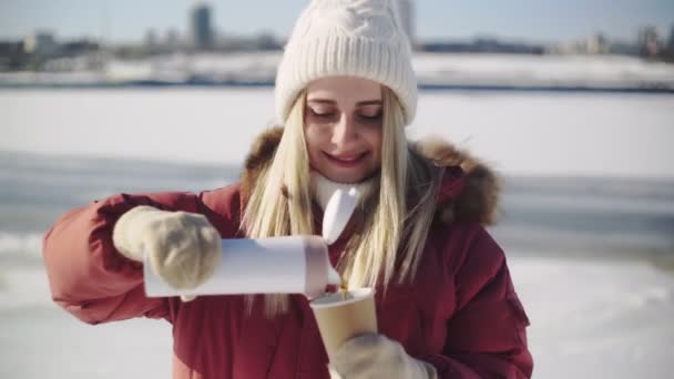 A woman pours tea fron thermos to cup in a snowy forest. A beautiful girl wants to warm herself in the winter outdoors with a mug of warm drink. Christmas Holidays — Stock Video