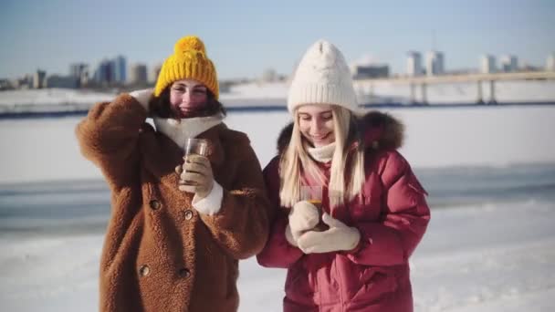 Две девушки в вязаных шляпах позируют с глинтвейном или стаканами для чая — стоковое видео