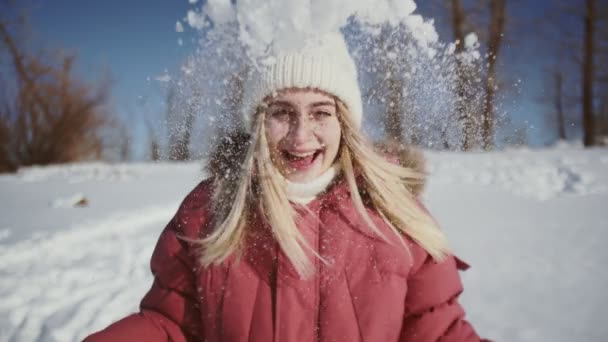 Beautiful woman in white knitted hat and red winter jacket throws up snow — Stock Video